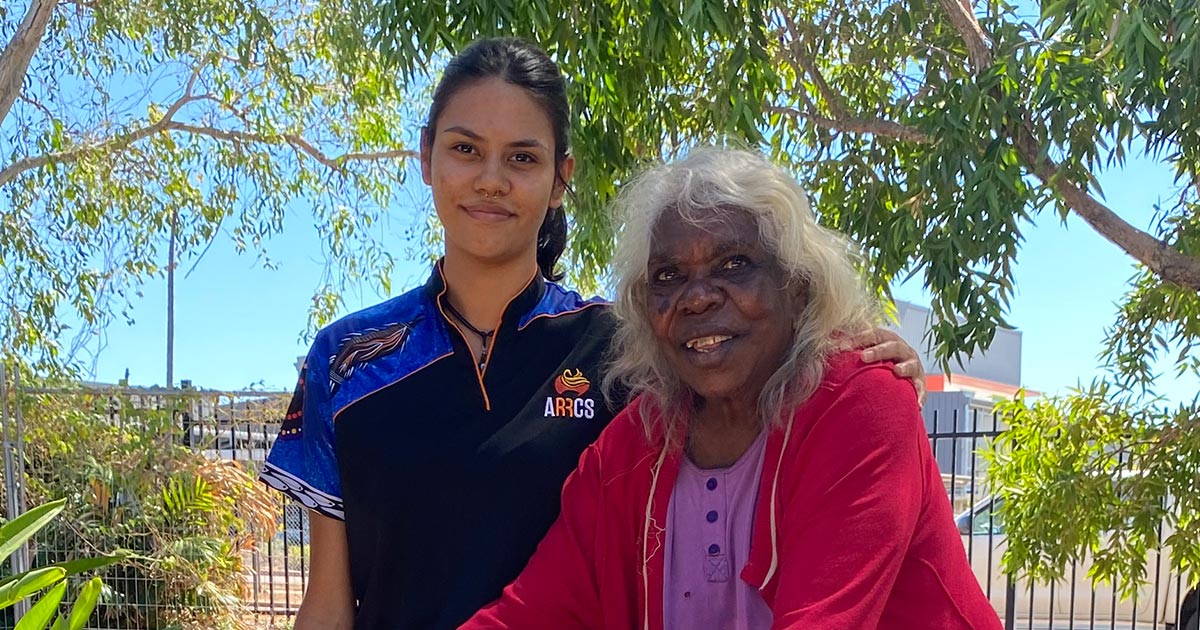 A young First Nations woman in ARRCS uniform rests her hand on the shoulder of a First Nations client.
