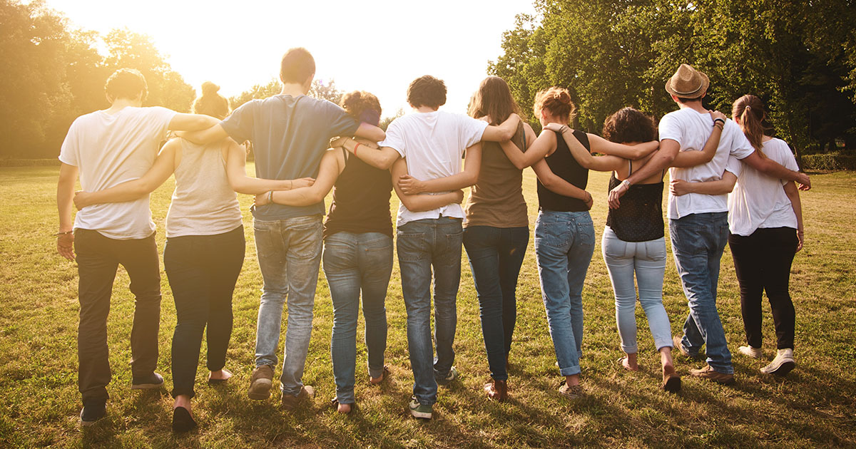 A group of 10 people walk into the sunset with their arms linked.