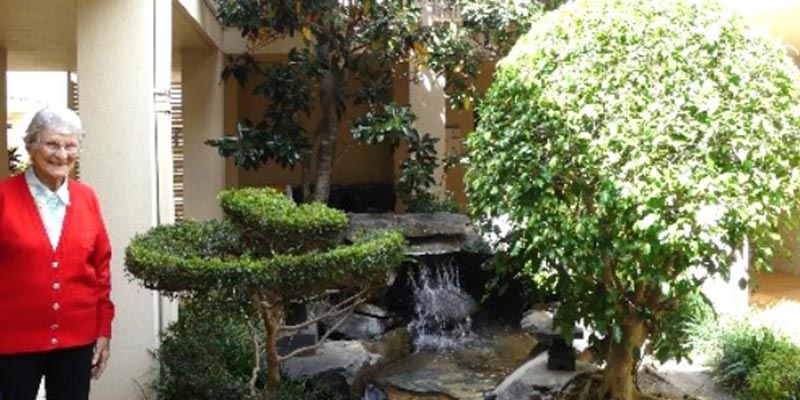 An elderly lady standing in front of he garden smiling at the camera