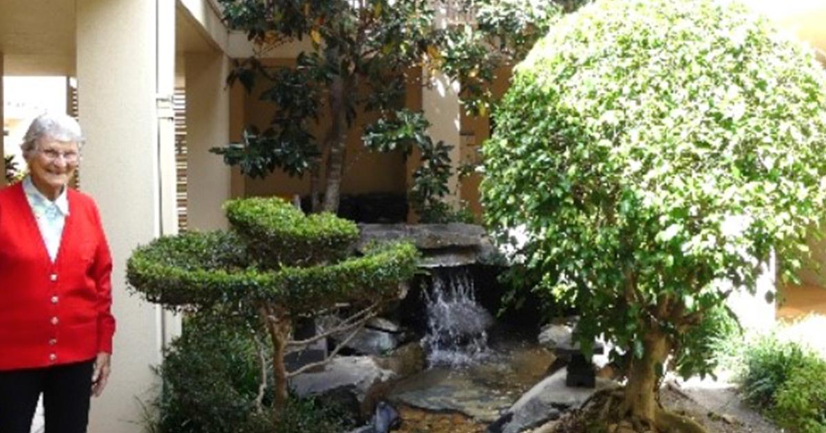 An elderly lady standing in front of he garden smiling at the camera