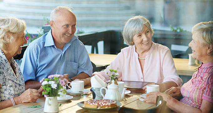 Elderly friends sitting around a table having morning tea and chatting