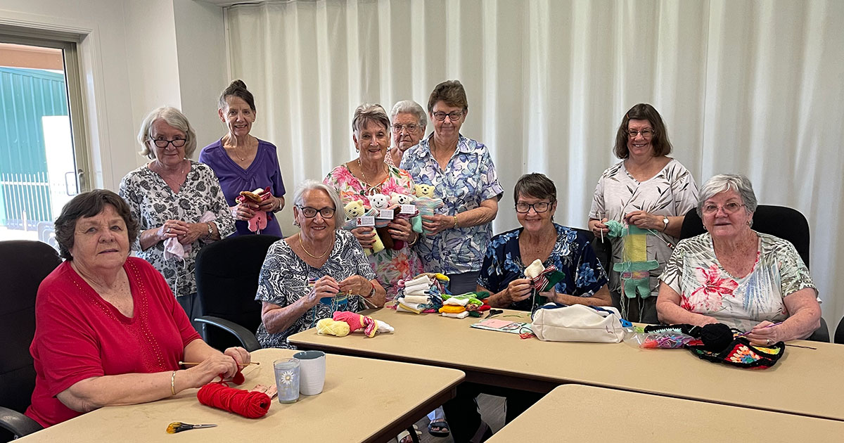 Carlyle Gardens knitting group sitting at tables smiling at camera