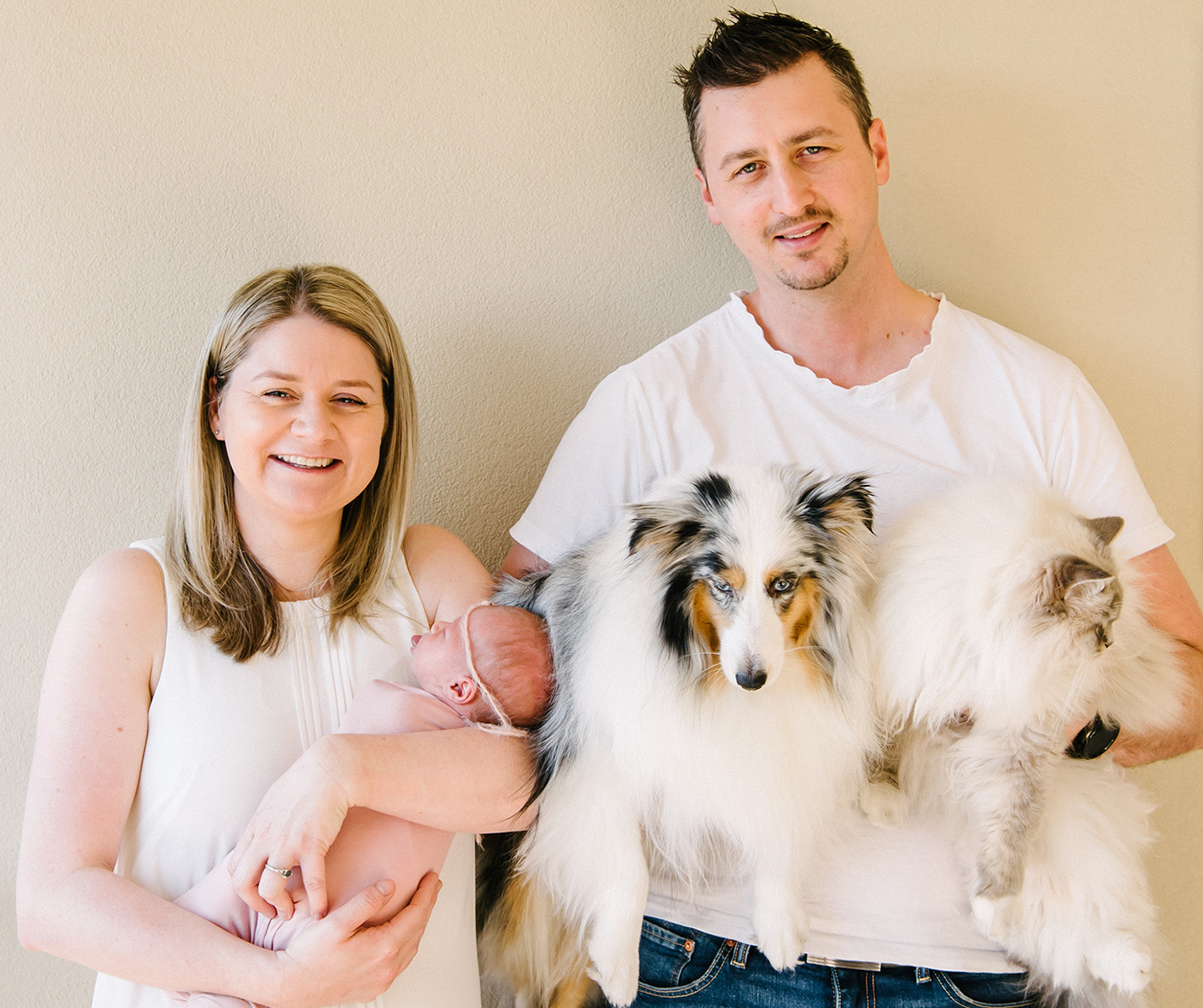 A smiling woman holding a new born baby next to a man holding a dog and a cat