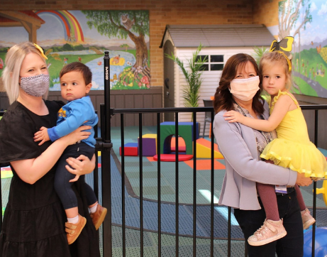 Two healthcare workers holding children, in front of a renovated playground